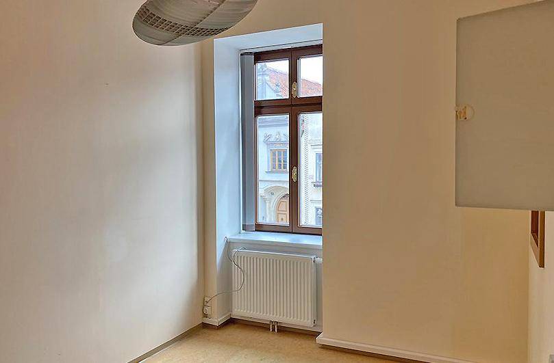 Heller Raum mit Holzboden und einem großen Fenster, das viel Tageslicht hereinlässt und Stadtblick bietet.