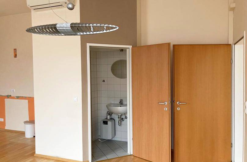 Wohnbereich mit Zugang zu einem kleinen Badezimmer mit Fliesen und Holztüren, funktional und gepflegt.