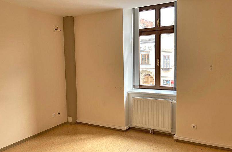 Unmöblierter Raum mit Holzboden, großem Fenster und Blick auf die umliegenden Gebäude der Stadt.