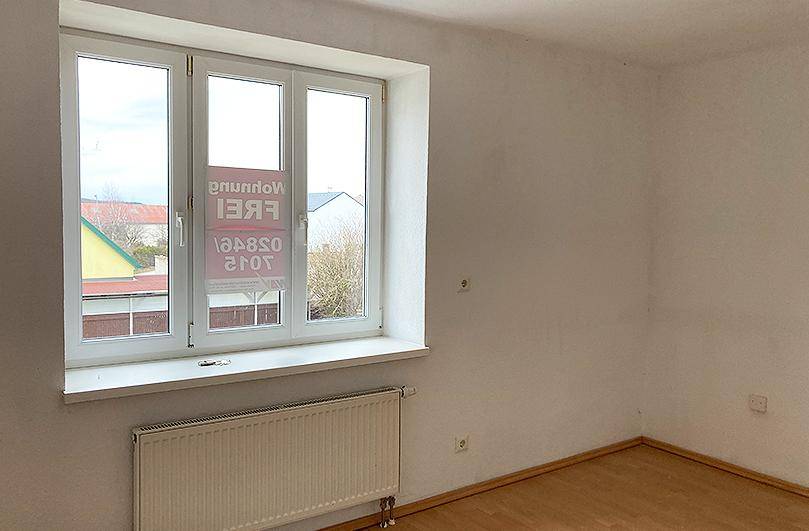 Unmöbliertes Zimmer mit Laminatboden und einem großen Fenster, das viel Tageslicht hereinlässt.