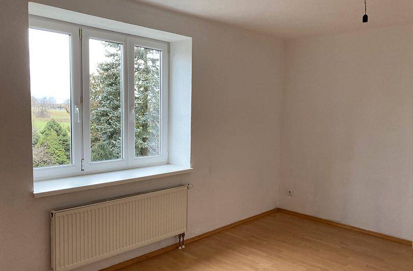 Helles Zimmer mit Laminatboden und einem Fenster, das einen ruhigen Blick ins Grüne bietet.
