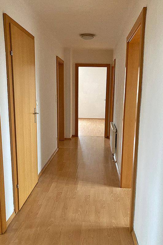 Langer, heller Flur mit Laminatboden und mehreren Holztüren, der die verschiedenen Räume verbindet.