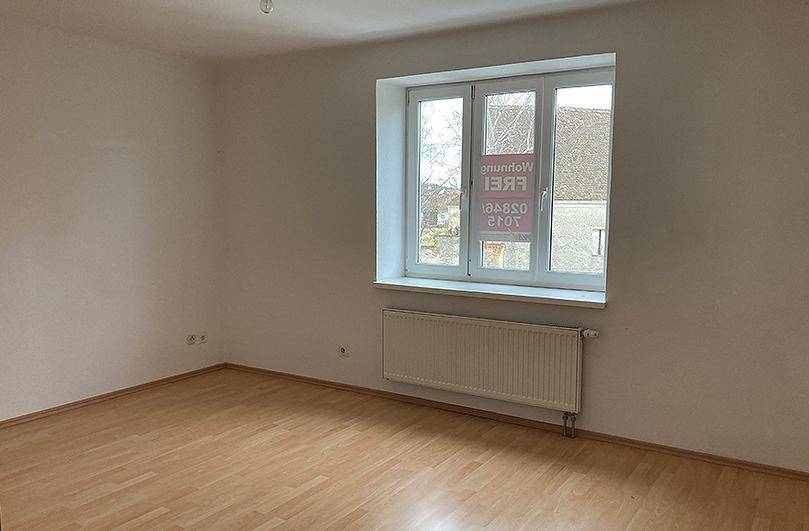 Leeres Zimmer mit Laminatboden, großem Fenster und Heizkörper, bereit zur individuellen Gestaltung.