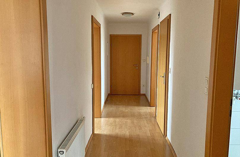 Heller Flur mit Laminatboden, weißen Wänden und mehreren Holztüren, die zu den Zimmern führen.