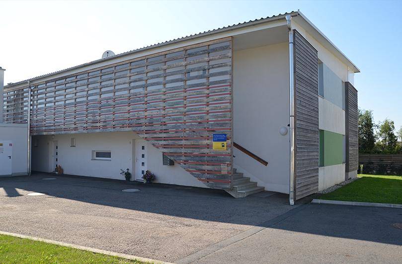 Rückseite des modernen Gebäudes mit Holzlamellenfassade und Außentreppe zum oberen Stockwerk.