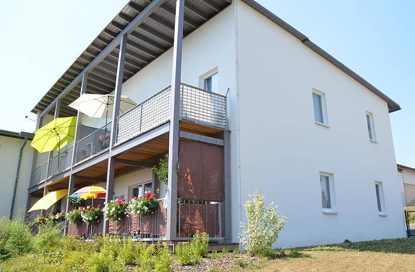 Seitenansicht des Gebäudes mit mehreren Balkonen, Sonnenschirmen und einer gepflegten Grünfläche.