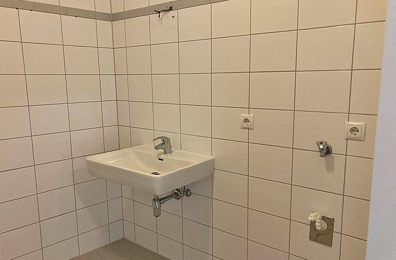 Modern gefliestes Badezimmer mit einem einzelnen Waschbecken und weißen Wandfliesen.