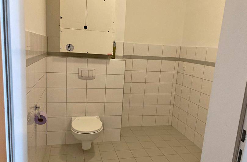 Separate Toilette mit Wand-WC, weißen Fliesen und einem Heizkessel an der Wand.