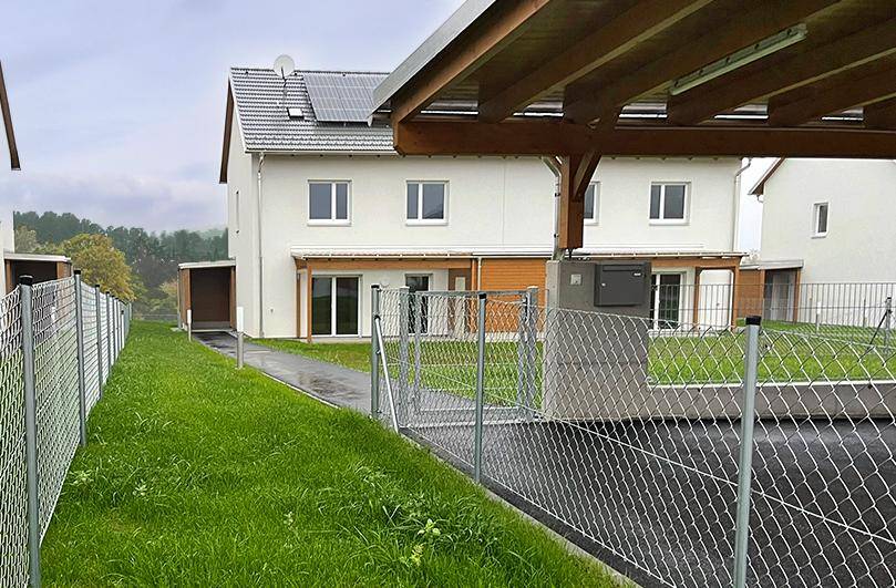 Seitenansicht des Doppelhauses mit Carport, Gartenbereich und Photovoltaikanlage auf dem Dach.
