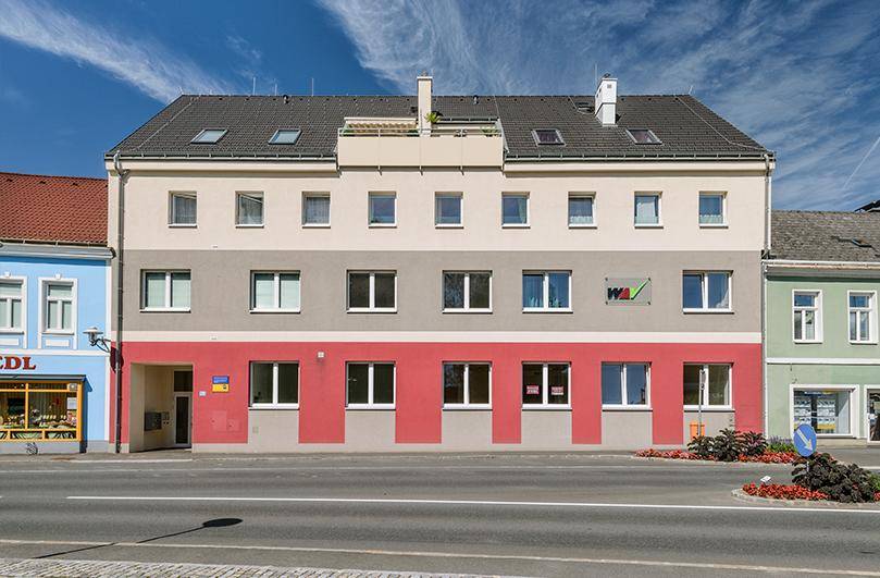 Mehrstöckiges Wohngebäude mit farbiger Fassade in Rot, Grau und Beige und Dachterrasse.