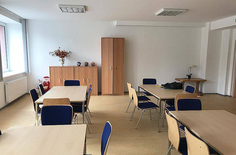 Heller Gemeinschaftsraum mit mehreren Tischen und Stühlen, ideal für Versammlungen oder Mahlzeiten.