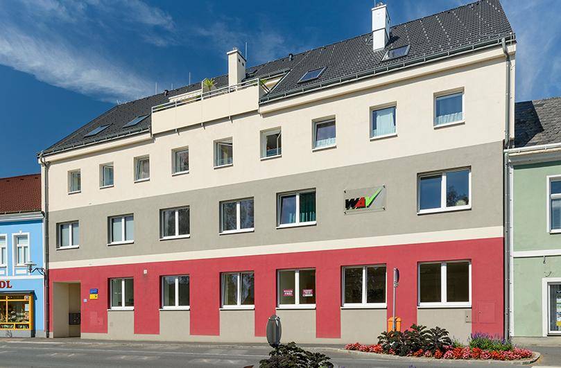 Ansicht des modernen Wohngebäudes mit mehrfarbiger Fassade und Dachterrasse unter blauem Himmel.