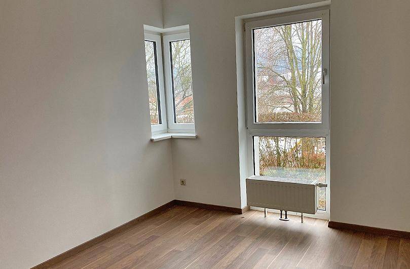 Leerer Raum mit großen Fenstern und Laminatboden, der viel Tageslicht bietet.