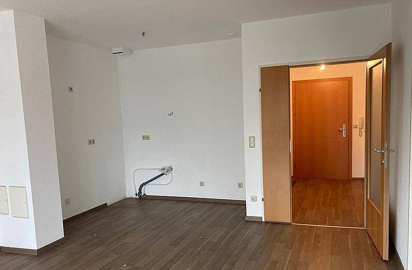 Leerer Raum mit Laminatboden und Anschlüssen, bereit für die Kücheninstallation.