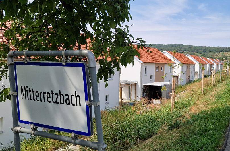 Ortseingangsschild von Mitterretzbach mit einer Reihe neuer Wohnhäuser im Hintergrund.
