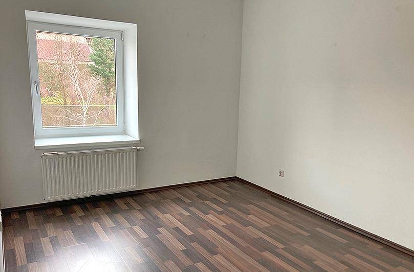 Helles Schlafzimmer mit Laminatboden und großem Fenster, das viel Tageslicht hereinlässt.
