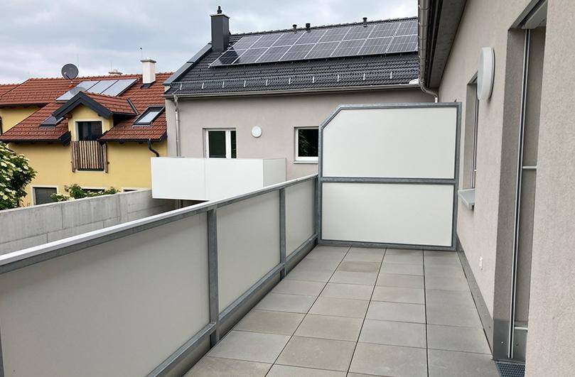 Heller Balkon mit Fliesenboden und moderner Brüstung, Solarpaneele auf dem Dach sichtbar.