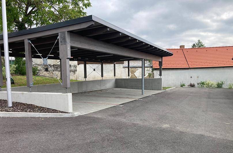 Überdachter Carport-Bereich mit Betonwänden und asphaltiertem Zufahrtsweg für Fahrzeuge.