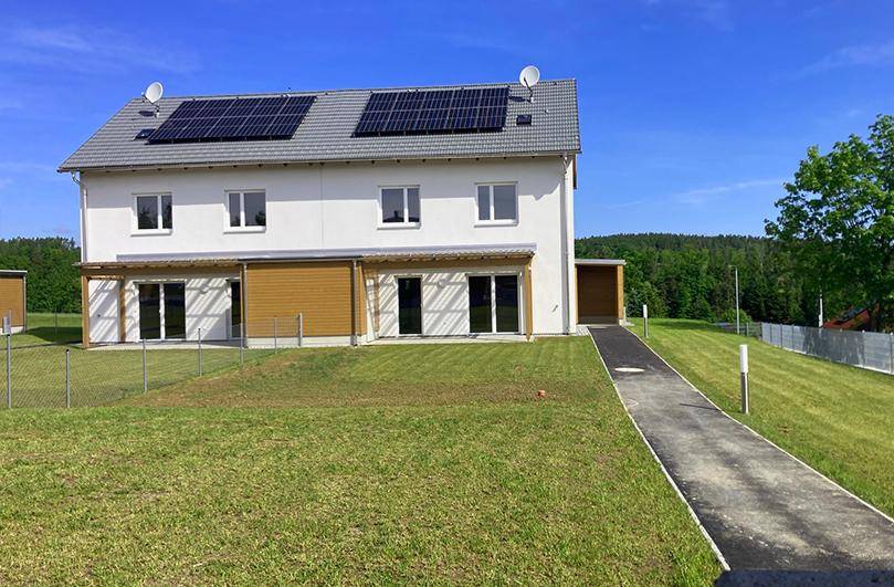 Moderne Doppelhaushälfte mit Photovoltaikanlage auf dem Dach und großem Gartenbereich.