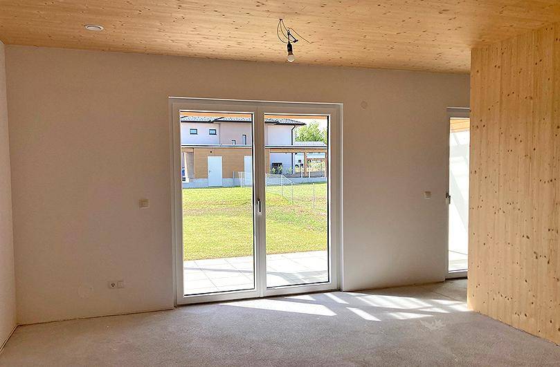 Heller, leerer Raum mit großer Schiebetür zum Garten und Holzbalkendecke.