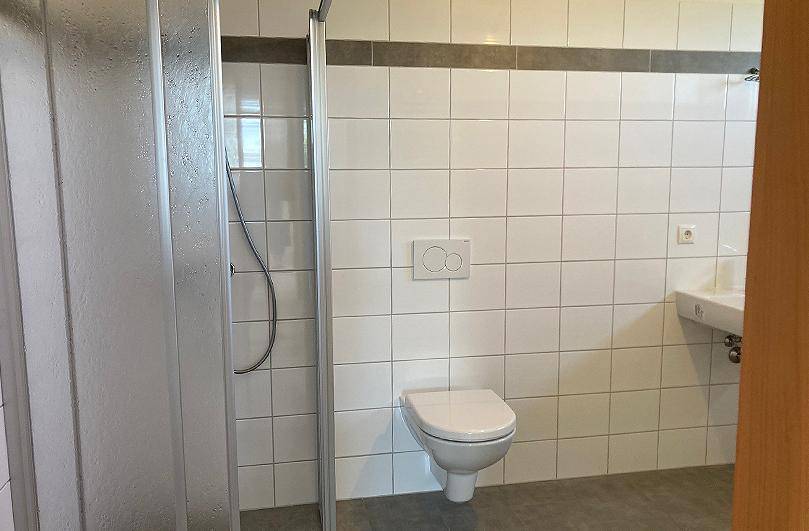 Modernes Badezimmer mit Dusche, wandhängendem WC und weißen Fliesen.