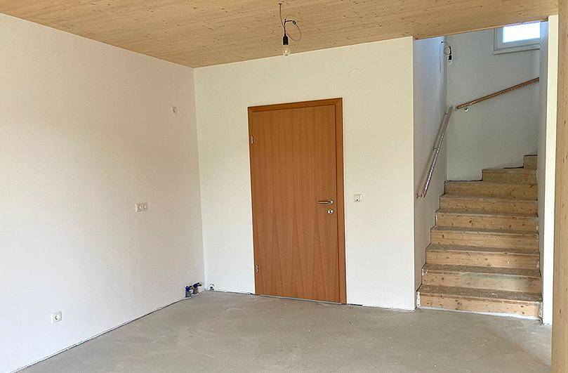Eingangsbereich mit Holztreppe und Holzbalkendecke in einem Neubau.