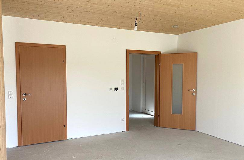 Heller Raum mit mehreren Türen und Holzbalkendecke, bereit für den Erstbezug.
