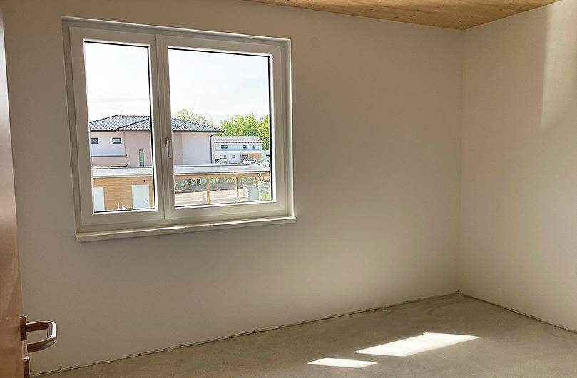 Leerer Raum mit großem Fenster und Blick auf die Nachbarhäuser und den Garten.