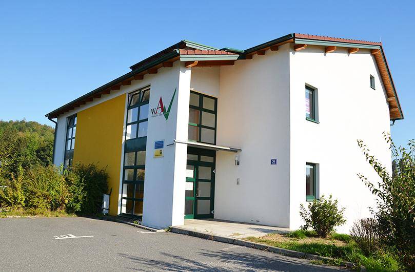 Eingangsbereich eines modernen Gebäudes mit weißer und gelber Fassade sowie großen Fenstern.