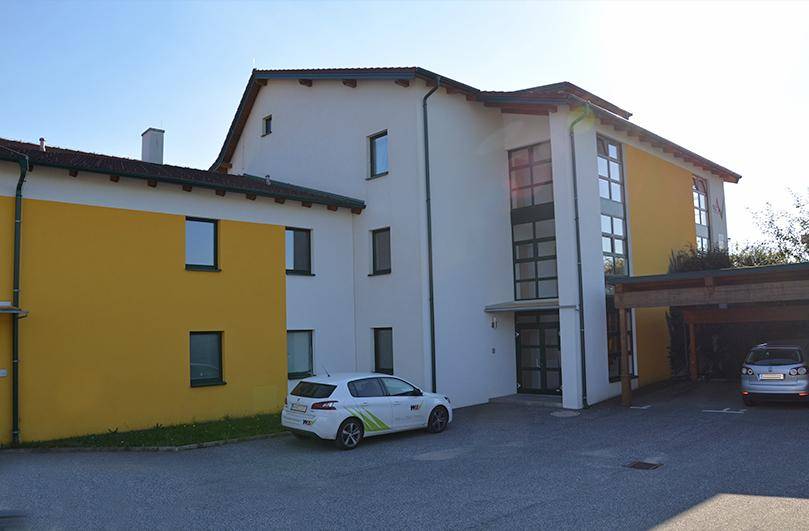 Ansicht des Gebäudes mit Parkplätzen, einem Carport und einer Mischung aus weißer und gelber Fassade.