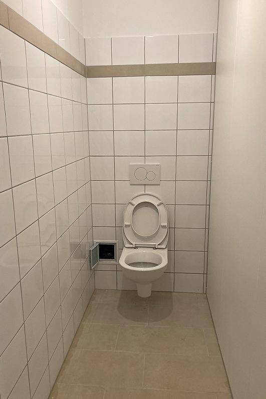 Separate Toilette mit Wand-WC und weißen Fliesen, in neuwertigem Zustand.