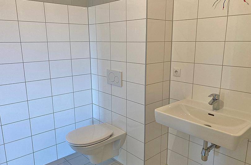 Modernes Badezimmer mit weißen Fliesen, wandhängendem WC und einem einzelnen Waschbecken.