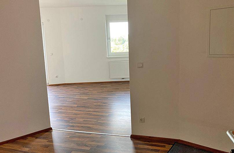 Heller Flur mit Laminatboden und weißen Wänden, der zu einem weiteren Raum führt.