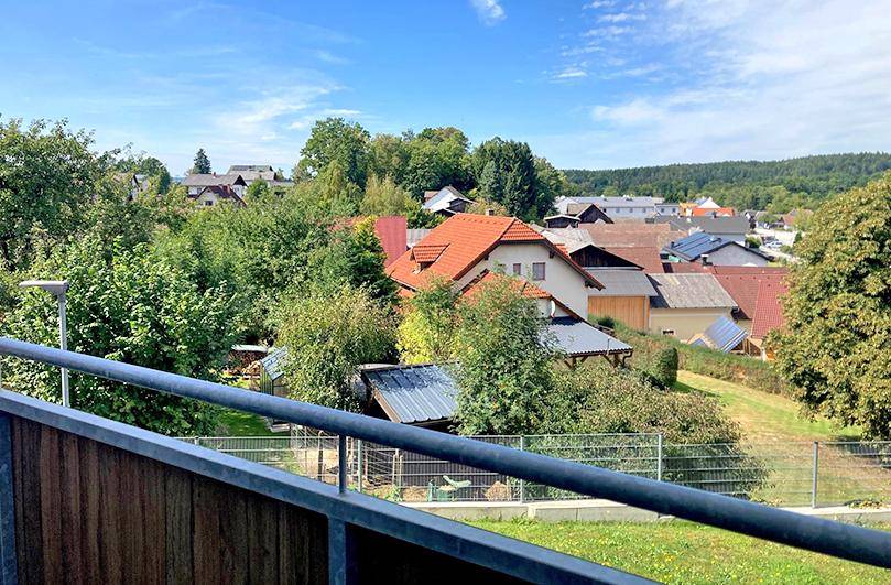 Weitblick vom Balkon über eine Siedlung mit roten Dächern und viel Grün in der Umgebung.