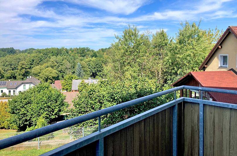 Schöner Ausblick vom Balkon auf grüne Bäume und die umliegende Landschaft unter blauem Himmel.