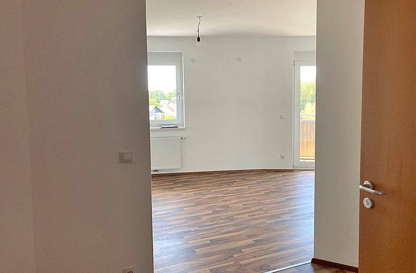 Heller Wohnraum mit Laminatboden und Zugang zu einem Balkon oder einer Terrasse.