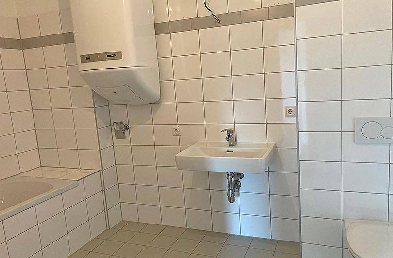 Gefliestes Badezimmer mit Badewanne, Waschbecken und Toilette, ausgestattet mit einem Warmwasserboiler.