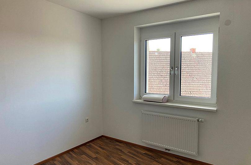 Helles Schlafzimmer mit Laminatboden, weiß gestrichenen Wänden und einem Fenster mit Ausblick.