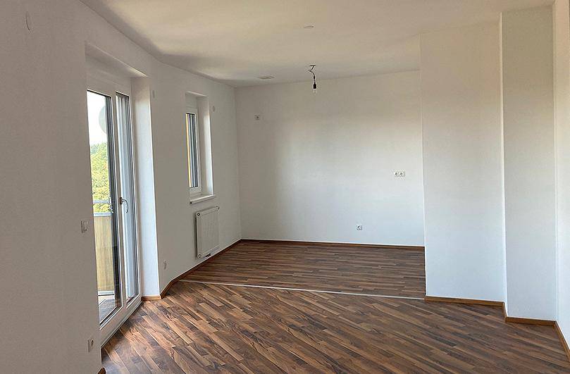 Lichtdurchfluteter Wohnraum mit Laminatboden, weiß gestrichenen Wänden und Balkonzugang.