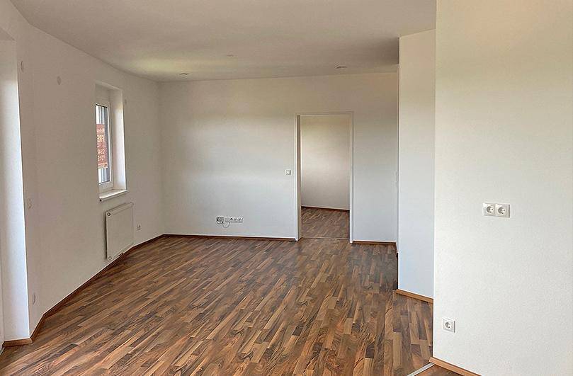Lichtdurchfluteter Wohnraum mit Laminatboden und weiß gestrichenen Wänden, bietet Zugang zu weiteren Räumen.