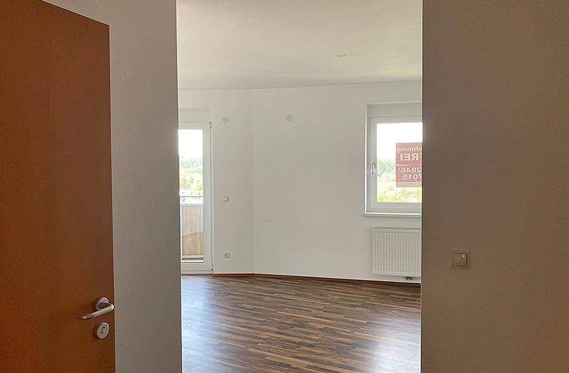 Heller Wohnraum mit Laminatboden, weiß gestrichenen Wänden und Zugang zu einem Balkon.