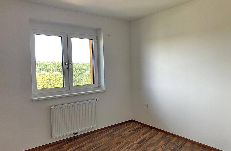 Helles Schlafzimmer mit Laminatboden, weiß gestrichenen Wänden und einem Fenster mit grüner Aussicht.