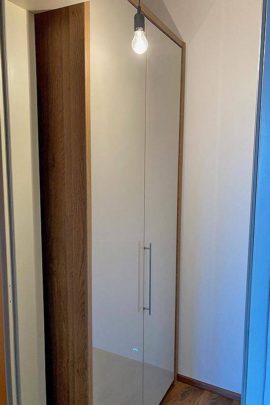 Moderner Einbauschrank mit glänzenden Türen und Holzrahmen in einem hellen Flurbereich.