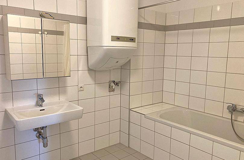 Badezimmer mit weißen Fliesen, Badewanne, Waschbecken und einem Spiegelschrank, in gutem Zustand.