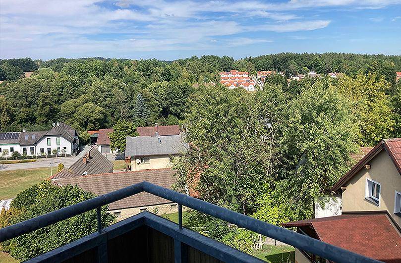 Panoramablick vom Balkon auf eine weite grüne Landschaft mit Wäldern und Häusern unter blauem Himmel.