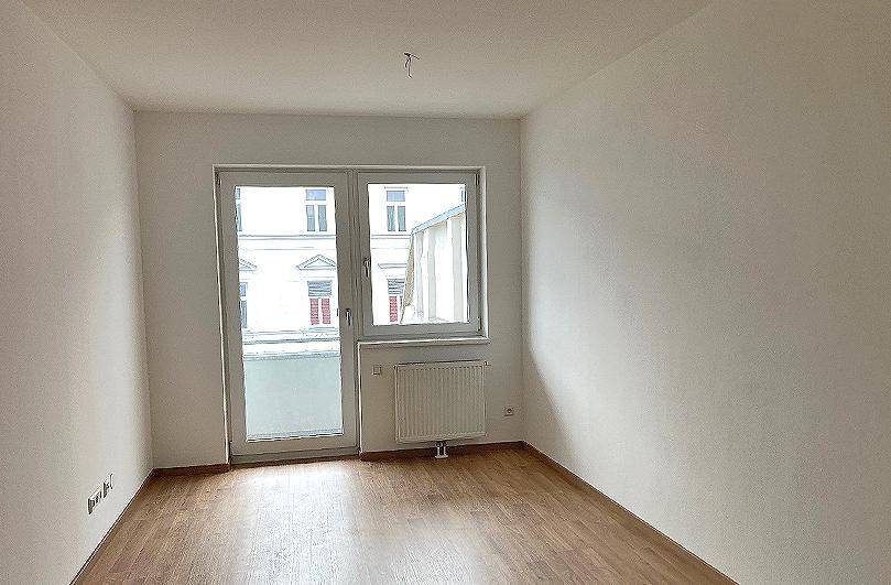 Heller Raum mit Laminatboden und Zugang zu einem französischen Balkon oder großen Fenster.