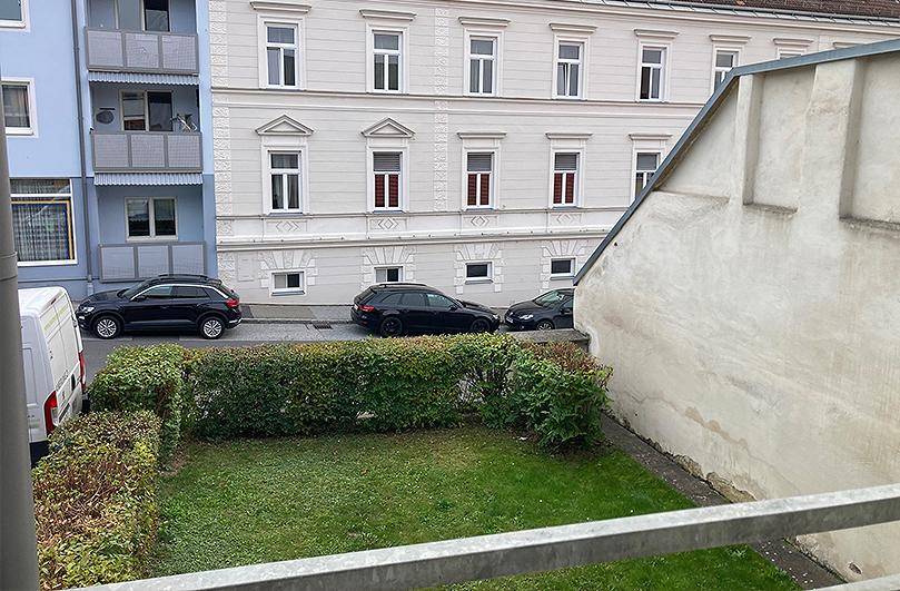 Kleiner Gartenbereich mit Hecke und Blick auf ein gegenüberliegendes Gebäude von einem Balkon.