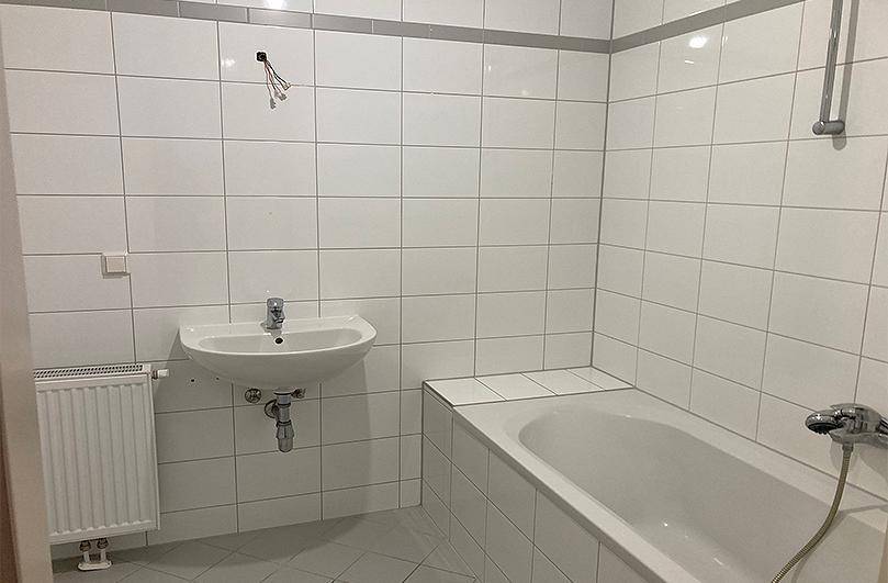 Gefliestes Badezimmer mit Badewanne, Waschbecken und Heizkörper in weißer Ausführung.