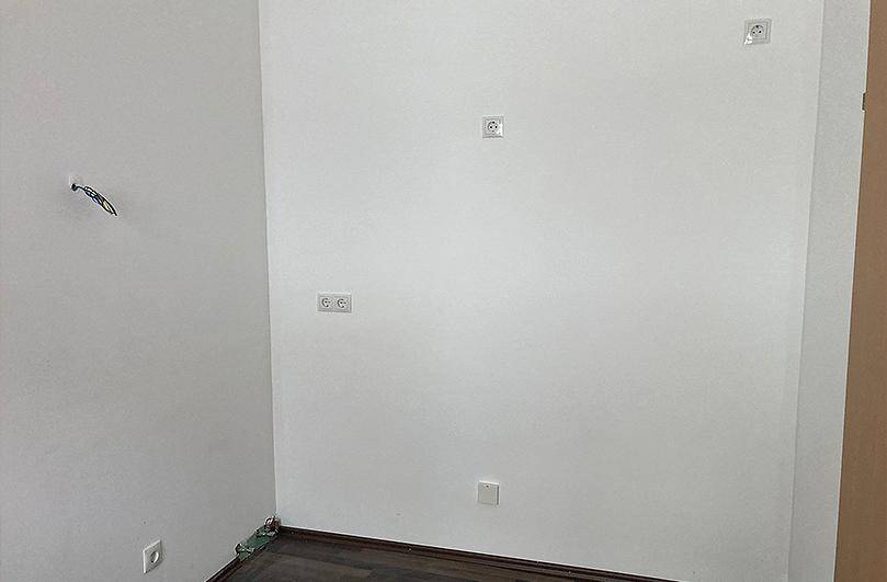 Leerer Raum mit weißen Wänden, dunklem Laminatboden und mehreren Steckdosen.