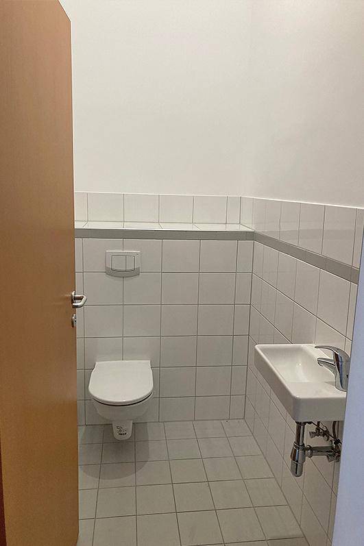 Modern geflieste Gästetoilette mit wandhängendem WC und kleinem Waschbecken.